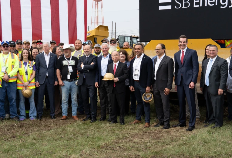 Group of SB Energy team members, project partners, and construction personnel gathered at the Ports Technology Campus groundbreaking event with construction equipment in the background.